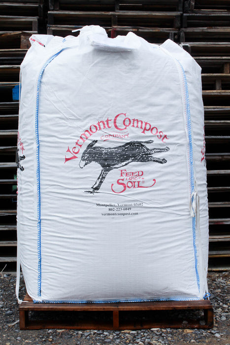 A large white bulk bag of Vermont Compost Company Soil, printed with a black donkey logo and red text, sitting on a wooden pallet in front of stacked pallets.