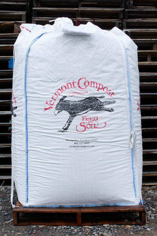 A large white bulk bag of Vermont Compost Company Soil, printed with a black donkey logo and red text, sitting on a wooden pallet in front of stacked pallets.