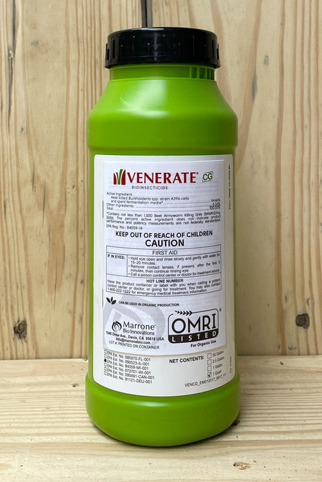 A green plastic bottle of Venerate with a black cap, standing on a wooden surface against a light wood panel background.