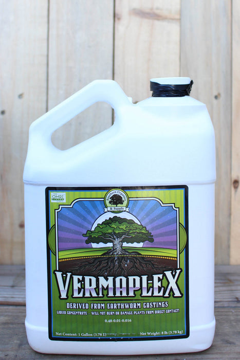 A large white plastic jug of Vermaplex with a colorful label featuring a tree, set against a rustic wooden background.