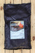 A large black plastic bag of VRD Volcanic Rock Dust, featuring a white and blue label with an illustration of a volcanic landscape, laid flat on a light-colored wooden plank surface.