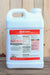 A white plastic jug of Weed Zap herbicide with a large red and black label, standing on a wooden surface against a wooden plank background.