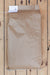A brown kraft paper bag of winter rye with a white paper tag attached at the top, laid flat on a light wood plank surface.