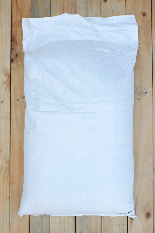A large white woven sack of zeolite laid flat on a light natural wood plank surface.