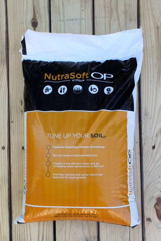 A bag of NutraSoft OP WP fertilizer, displayed on a light-colored wooden plank surface. The packaging features a black top section with white and orange branding, and a large orange lower section with white text.